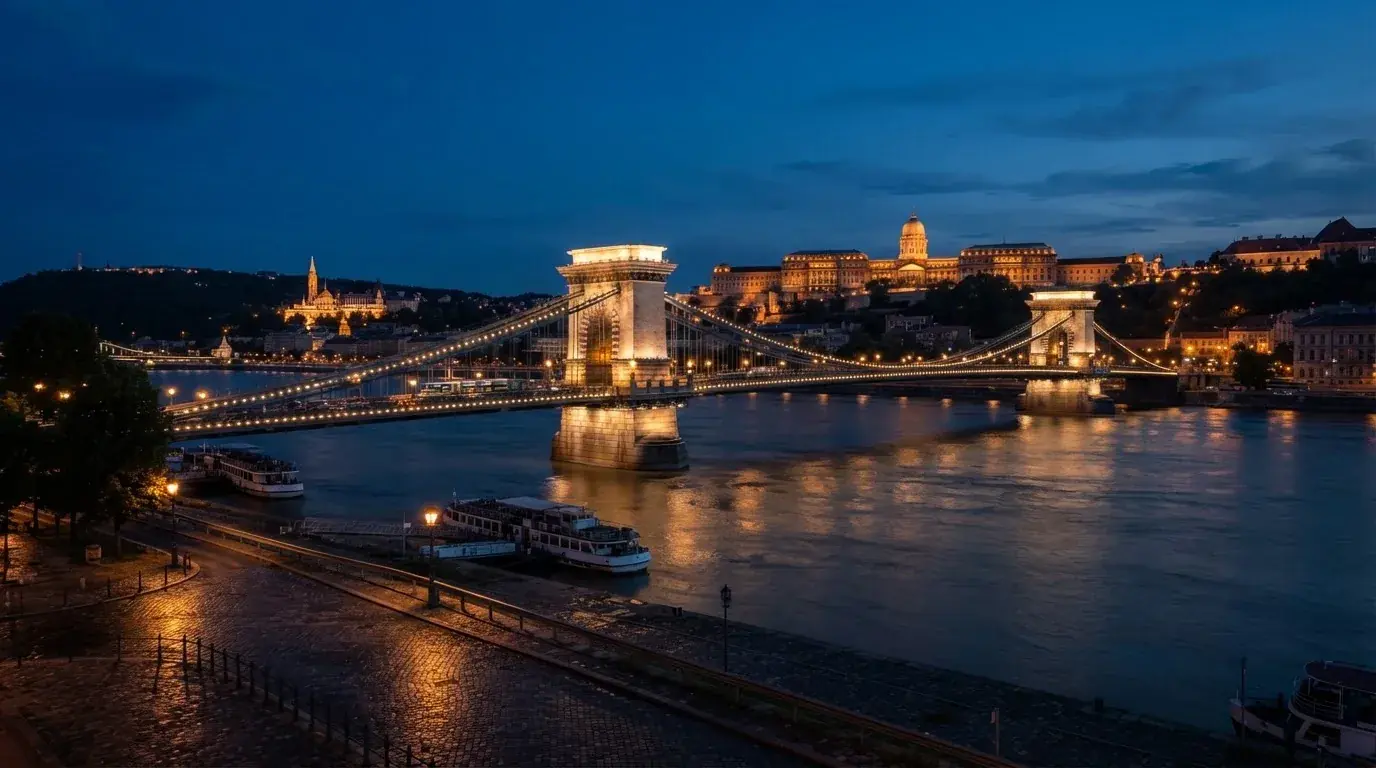 A budapesti Lánchíd esti fényekben a Duna fölött, a háttérben a budai Vár, forgalom nélküli rakpart.